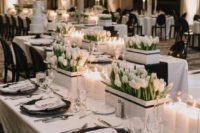 a stylish wedding tablescape with black chargers, white tulips in boxes and a white tablecloth