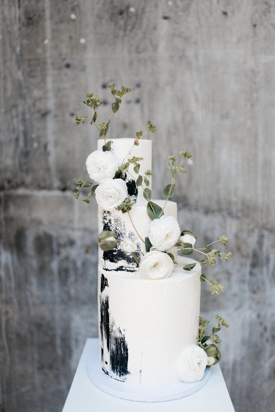 a white wedding cake with black brushstrokes and white ranunculus and greenery