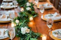 an uncovered table with a long greenery and white bloom garland plus candles that create a cool rustic feel