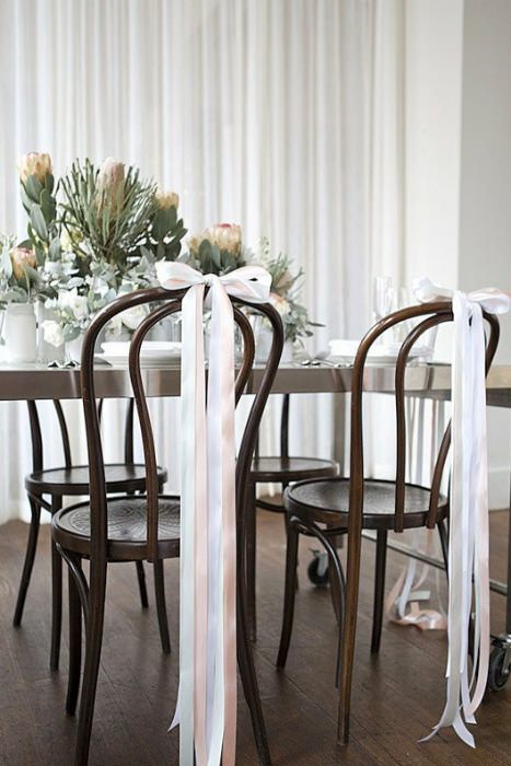 dark-stained chairs with blush and white ribbon bows on top are amazing for a chic and elegant wedding with a delicate touch of color