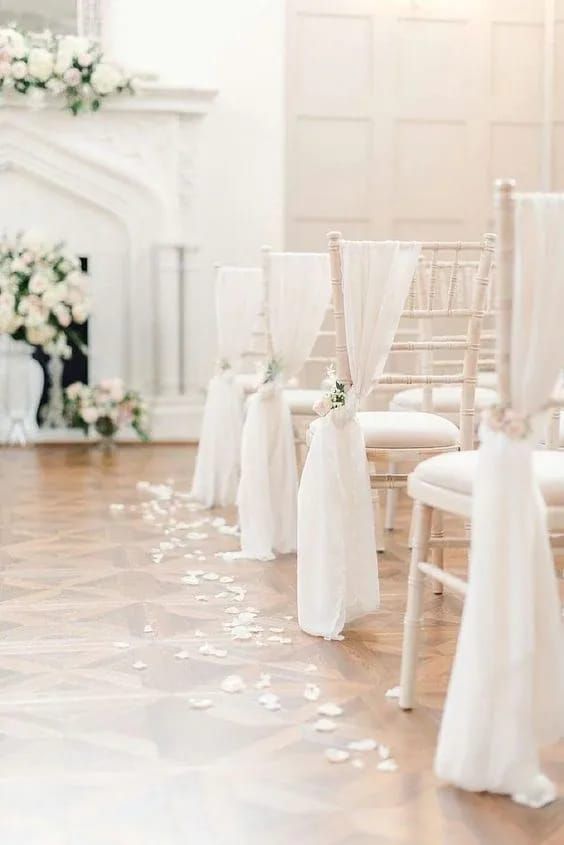 ethereal wedding chair decor with white fabric, white blooms and greenery and petals on the floor is amazing