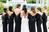 the bridesmaids wearing black maxi dresses with pearl statement necklaces and the bride wearing white