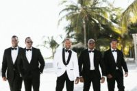 the groom in a white tux and the groomsmen wearing black tuxes for an elegant formal wedding