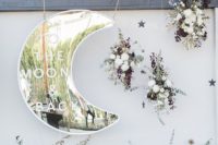 a beautiful wedding backdrop with a shiny silver moon, lush florals and dark and dried herbs and leaves