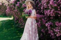 a blush A-line cap sleeve wedding dress with white lace appliques and a train plus a hat for a romantic spring garden wedding