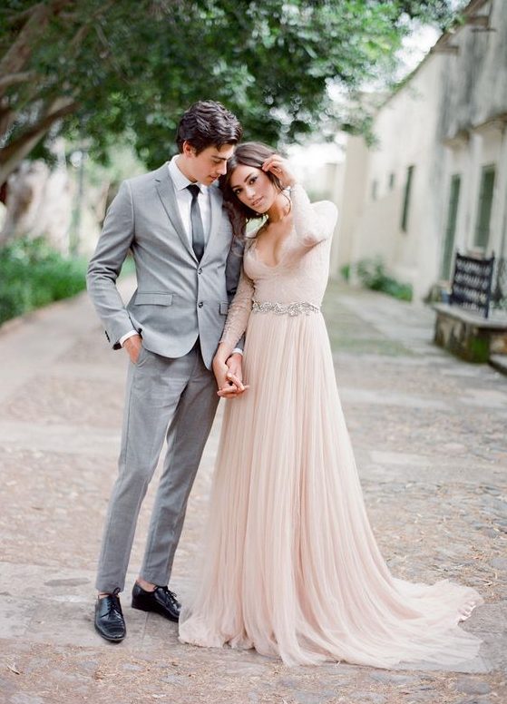 a blush A-line wedding dress with a lace bodice, a plunging neckline, long sleeves and a layered skirt plus a train