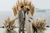 a boho wedding altar of pampas grass, pastel blooms and some foliage plus a sea view for a boho wedding