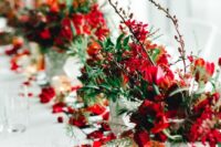 a bold red winter wedding table runner with bold red blooms, twigs and branches, greenery and petals on the world