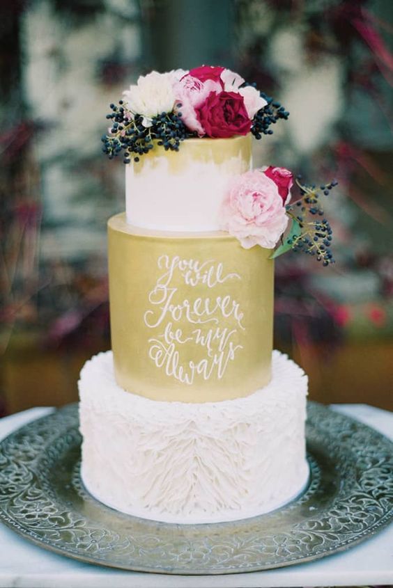 a bright and cool wedding cake with gold tiers and calligraphy, a ruffle tier, bright blooms and privet berries on top is a lovely idea for a fall wedding