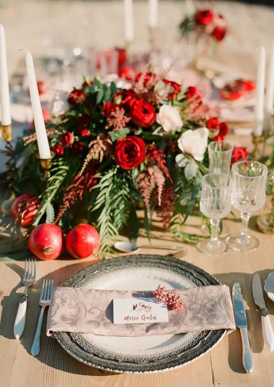 a bright wedding tablescape with pomegranates, greenery, white and red blooms and berries on the place setting