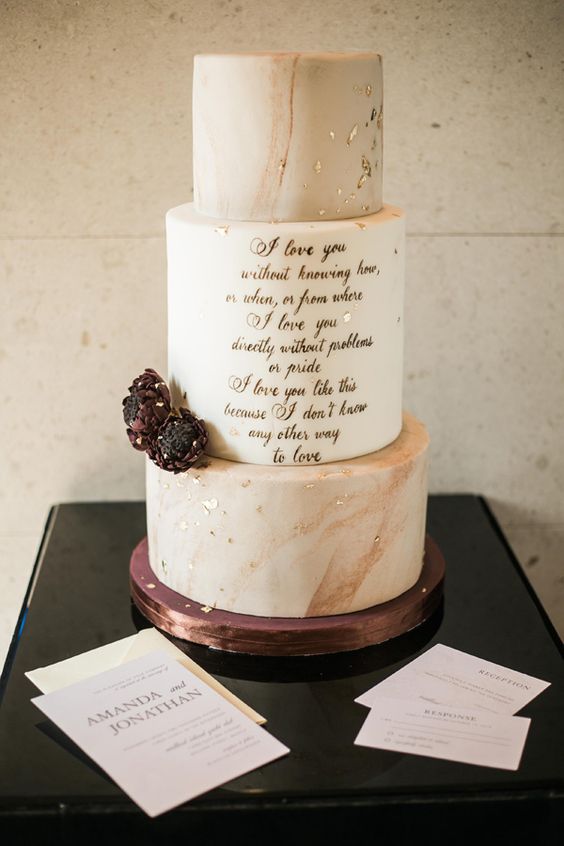 a chic and refined wedding cake with blush marble and white tiers, with gold leaf and gold love letters in the center, deep purple blooms