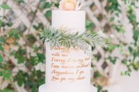 a chic and stylish wedding cake with a peachy and white tier, copper calligraphy love letters, greenery and a peachy bloom on top