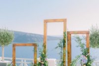 a chic wedding altar of wooden frames, blue and yellow blooms and lush greenery with a gorgeous sea view