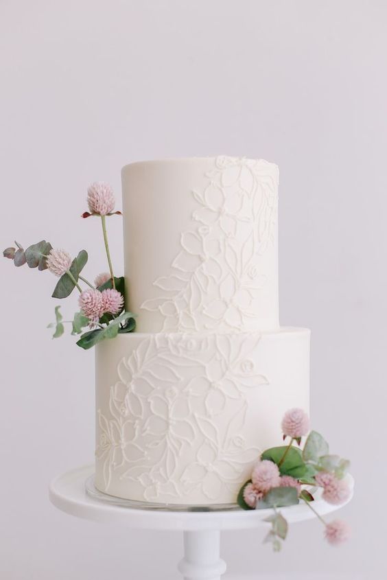 a chic white floral lace wedding cake decorated with blush blooms and greenery looks chic and modern