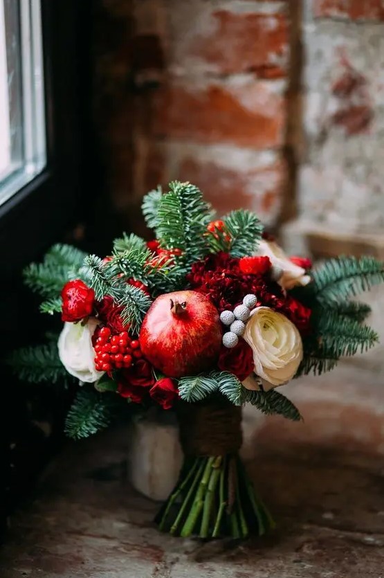 a cozy winter wedding bouquet of fir, red and white blooms, berries and pomegranates for a winter or Christmas wedding