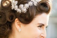 a fully curled wedding updo with a volume on top and a shiny flower hairpiece