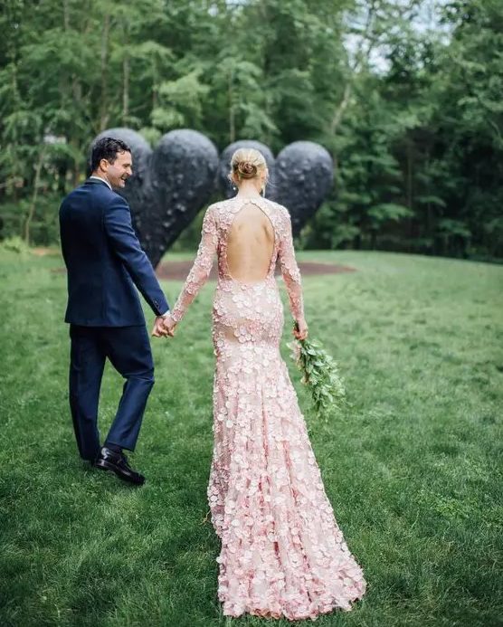 a light pink wedding dress with a cutout back, long sleeves fully covered with floral petals is a lovely and pretty idea