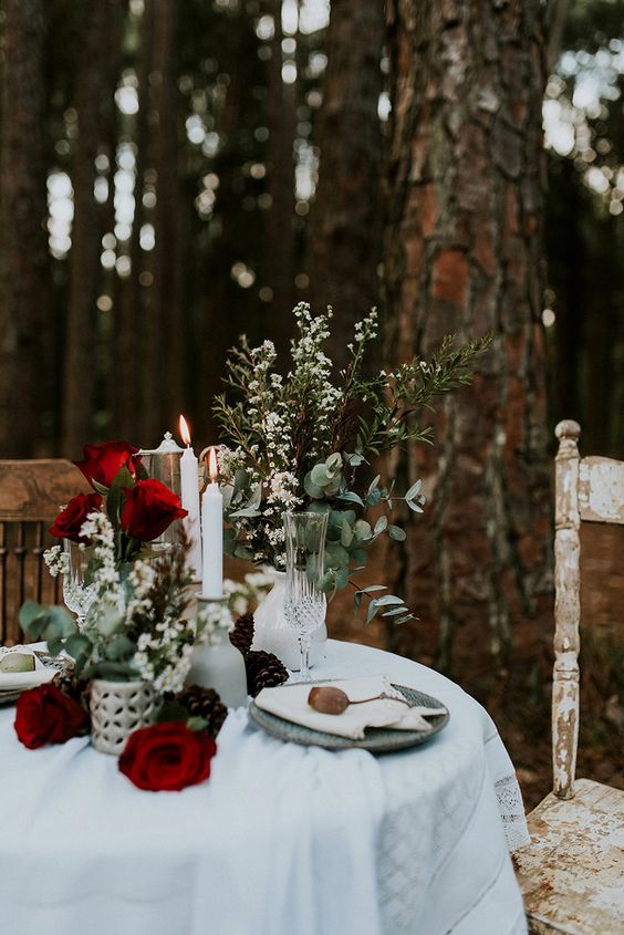 a lovely boho winter wedding tablescape with red roses, greenery and candles plus grey plates is a cool and chic idea