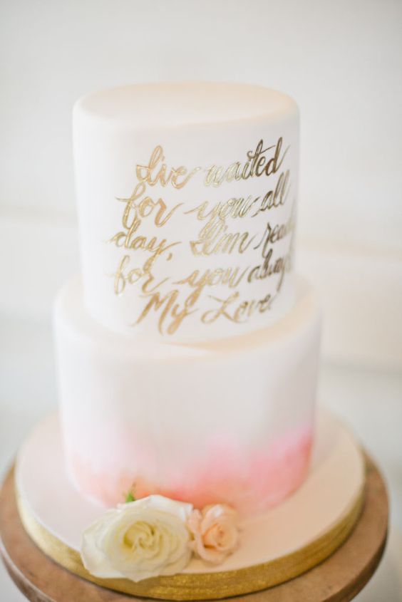 a lovely modern wedding cake with a pink watercolor tier, a white tier with a gold calligraphy love letter and some blooms