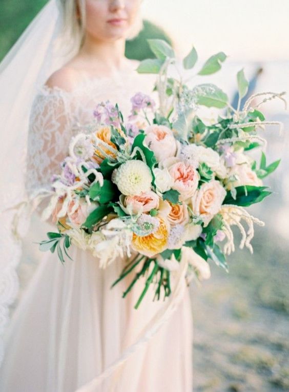 a lush oversized wedding bouquet in the shades of blush, muted yellow, mauve and cream plus greenery