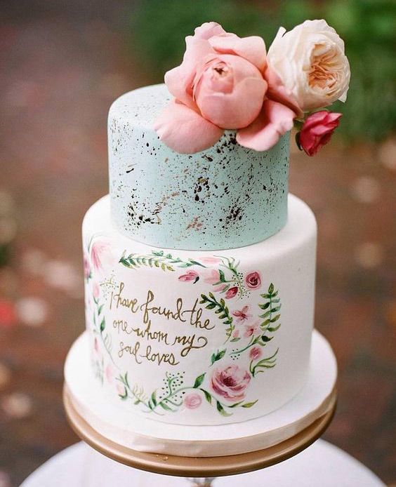 a pastel wedding cake with a light mint and speckle tier and a love letter with painted blooms plus some pink flowers on top