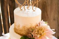 a pretty white and gold glitter wedding cake with greenery, berries and a pink dahlias, a gold glitter calligraphy cake topper