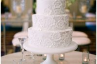 a purely white floral lace wedding cake accented with candles around is a sophisticated and elegant piece