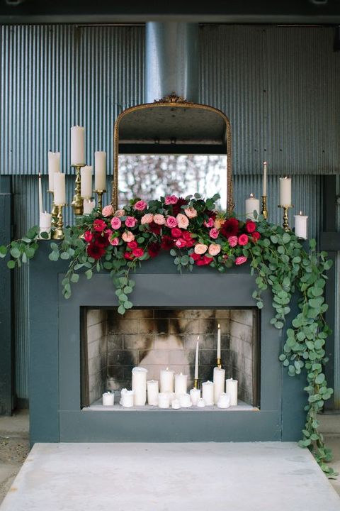 a refined modern fireplace as a wedding backdrop with pillar candles, bright lush florals and a large vintage mirror