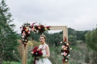 a refined wedding arch of a gold picture frame, bold burgundy, yellow and blush blooms and some foliage
