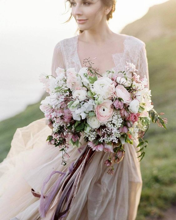 a romantic pastel wedding bouquet with white, blush and dusty pink blooms and long ribbons with a texture
