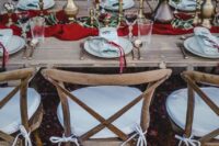 a stylish boho winter wedding tablescape with a red table runner and candles, blooms and greenery and neutral plates and napkins