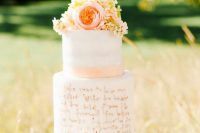 a white buttercream wedding cake with a plain and a love letter tier, peachy ribbon and peachy and neutral blooms plus calligraphy on top
