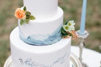 a white buttercream wedding cake with blue watercolors and blue love letters, neutral and bright blooms and greenery