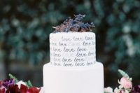 a white buttercream wedding cake with calligraphy LOVE letters on the tiers and privet berries on top is a cool idea for any refined wedding