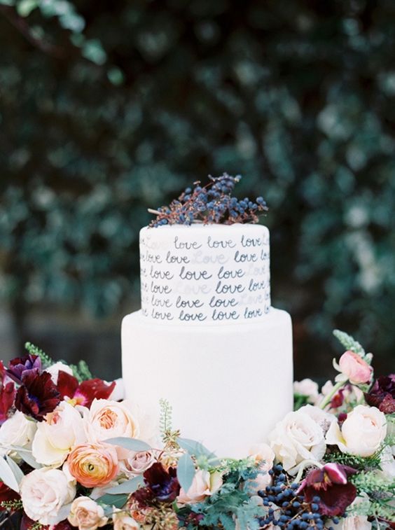 a white buttercream wedding cake with calligraphy LOVE letters on the tiers and privet berries on top is a cool idea for any refined wedding