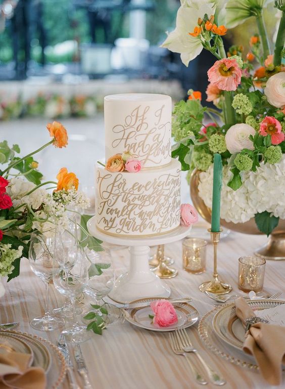 a white buttercream wedding cake with gold calligraphy and bright blooms is a chic and cool solution for spring or summer