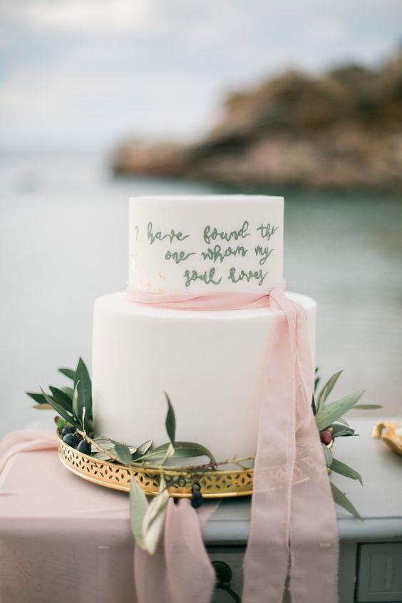 a white buttercream wedding cake with gold calligraphy on one tier and a pink ribbon tie is a dreamy idea for a sophisticated wedding