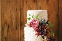 a white floral lace weddng cake decorated with burgundy and fuchsia plus bue fresh blooms for a more modern feel