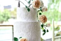 a white lace wedding cake topped with peachy blooms and some dark foliage that make it feel more modern and bold