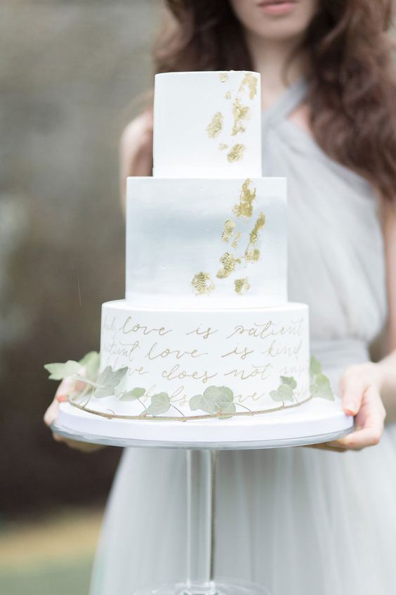a white wedding cake with a light grey tier, gold leaf, a love letter tier and greenery is a cool solution for a spring or summer wedding