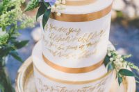 a white wedding cake with copper ribbon and gold calligraphy love letters on the tiers, a blue bloom and some flowers is a lovely idea for a spring wedding