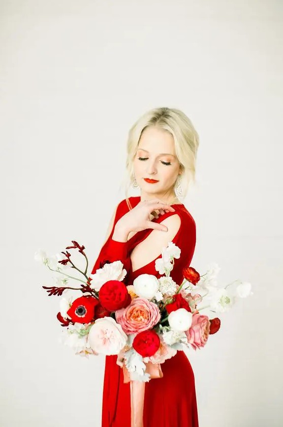a winter bride wearing a hot red dress with shoulder cutouts, a red lip and a bold red and white wedding bouquet