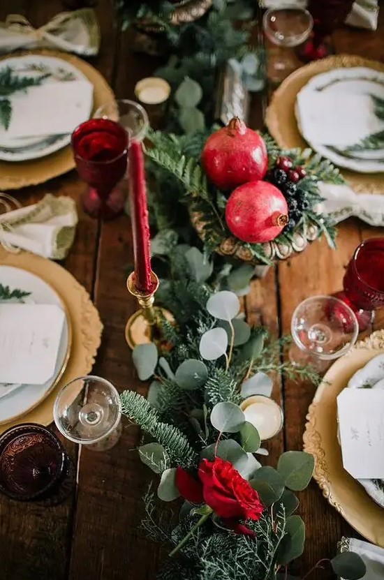 a winter wedding tablescape with a greenery and fir runner, pomegranates and berries, red candles and gold chargers