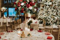 an elegant and chic Christmas wedding reception table with red napkins and a tall topiary wedding centerpiece with red and white blooms