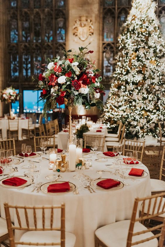 an elegant and chic Christmas wedding reception table with red napkins and a tall topiary wedding centerpiece with red and white blooms