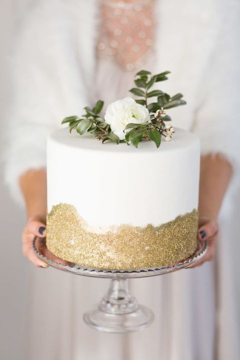 an elegant white and gold glitter wedding cake topped with a white bloom and greenery is a stylish idea for many weddings