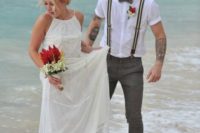 a beach groom’s look with a white shirt, striped suspenders, grey pants and a bright boutonniere