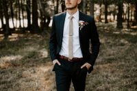 a black pantsuit, a white shirt, a tan skinny tie and a floral boutonniere are a chic and cool combo for a modern wedding