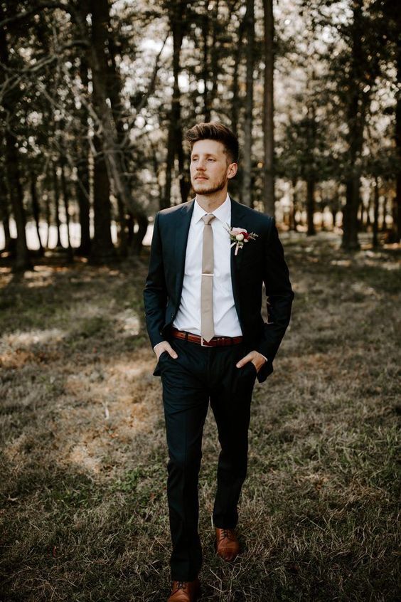 a black pantsuit, a white shirt, a tan skinny tie and a floral boutonniere are a chic and cool combo for a modern wedding