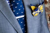 a bold and cool groom’s outfit with a blue and white checked shirt, a navy and white whale print tie, a grey blazer and a printed handkerchief